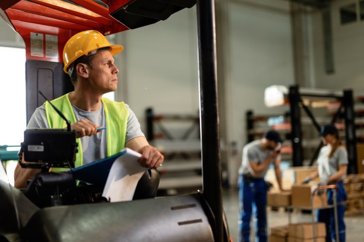 Forklift driver going through paperwork thinking something while working distribution warehouse.