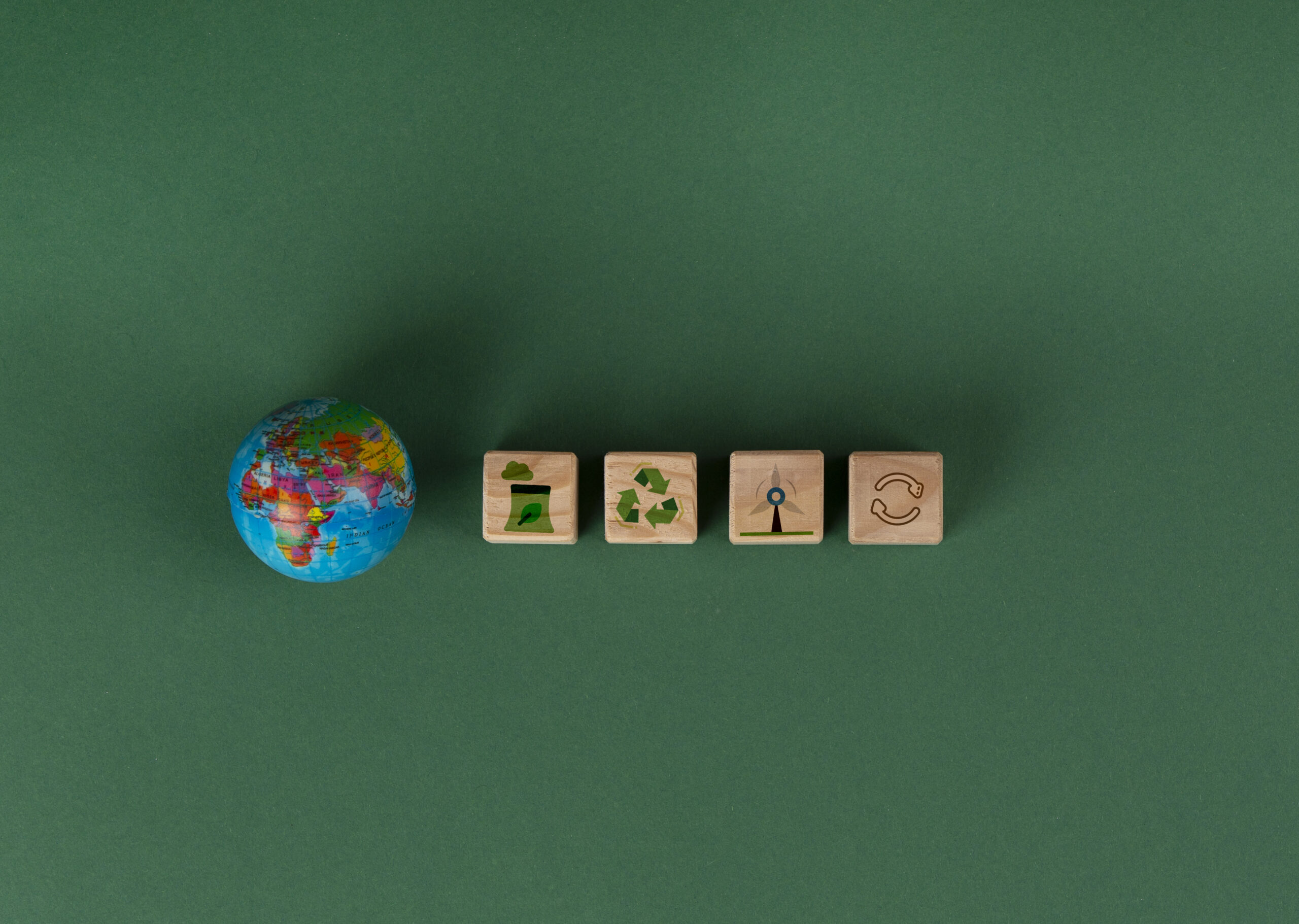 Sustainable development goals still life. Wooden blocks on a dark green background. Each block has a symbol that depicts an environmental image. Blocks proceeded by a small colourful globe.